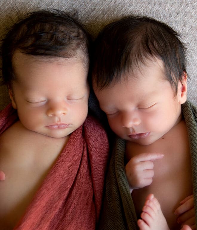 A couple of dark haired twin babies laying next to each other