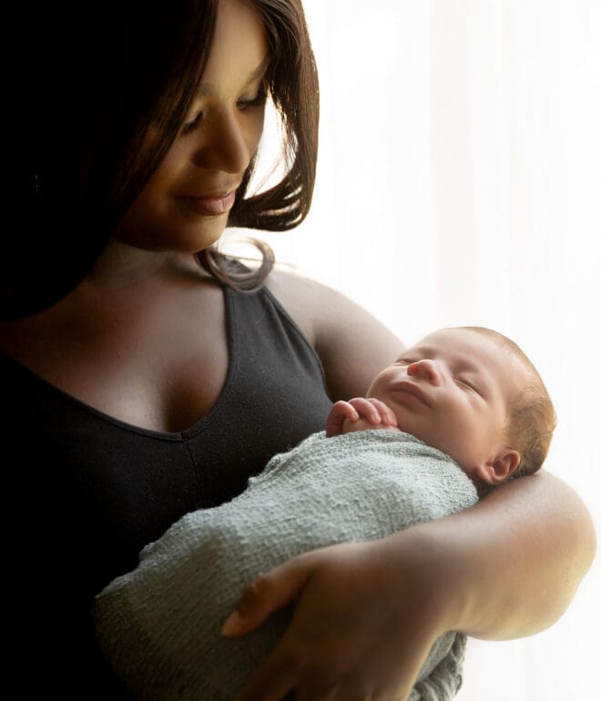 A woman, holding a swaddled baby in her arms while standing