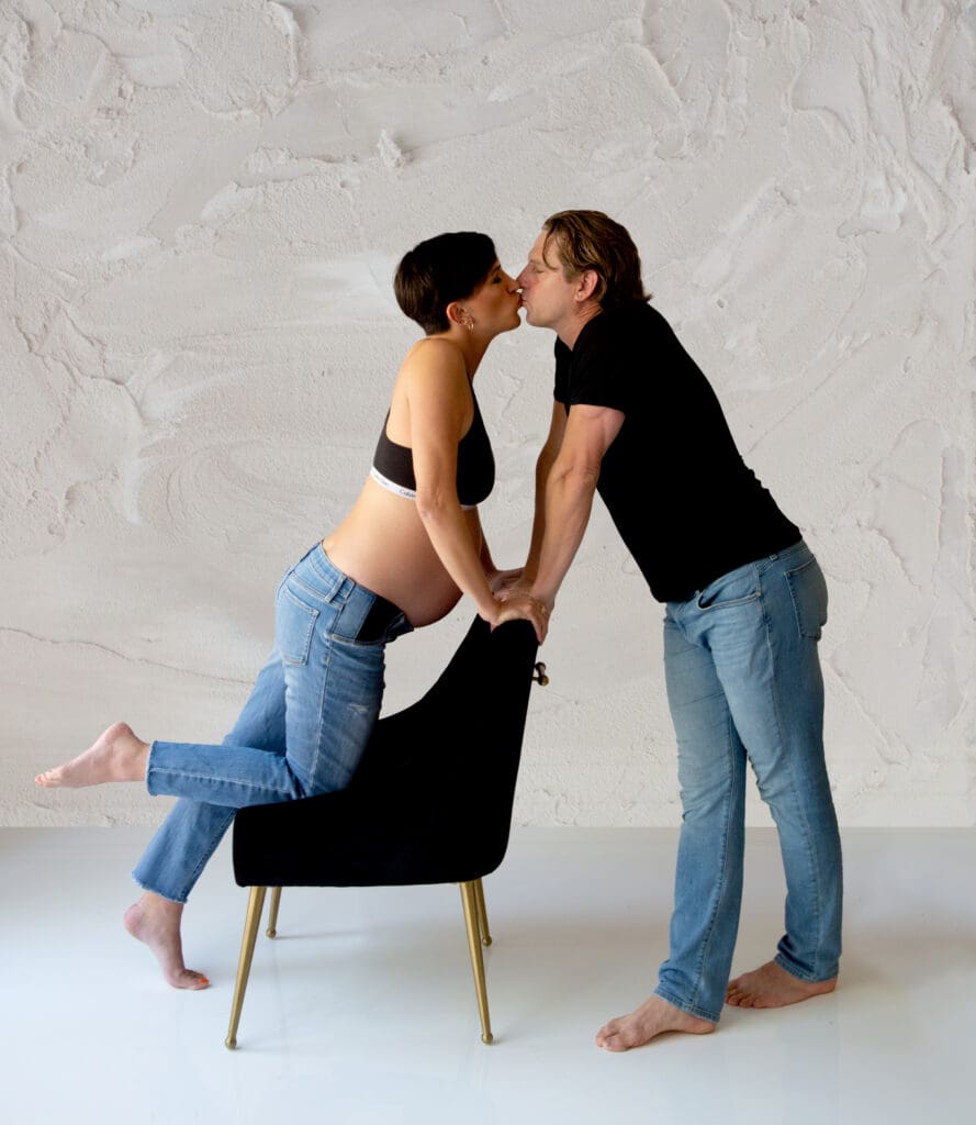 A man and pregnant woman leaning over a chair to kiss each other