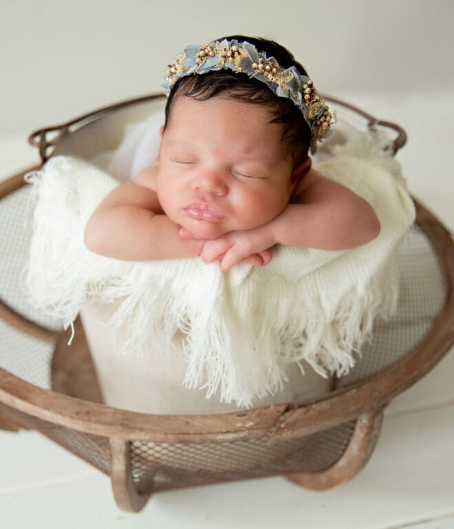 A newborn baby girl sleeping in a basket covered with white linens