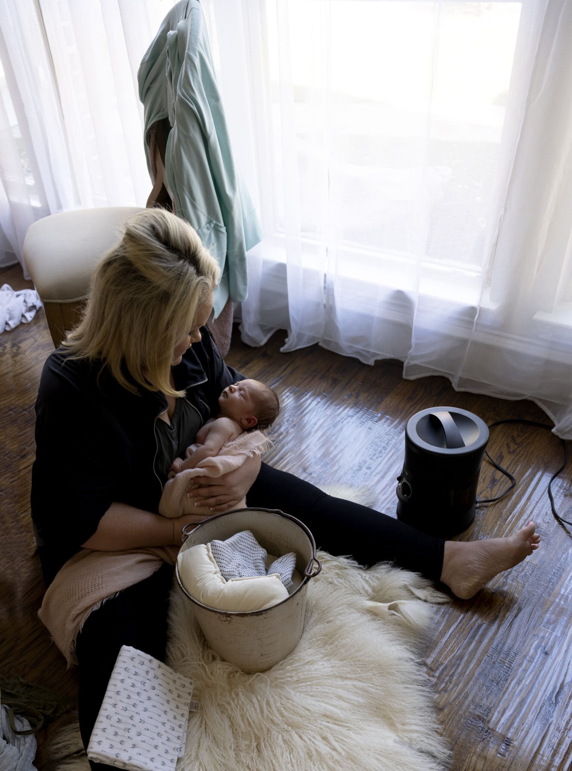 A woman sitting on a white rug on the floor holding a baby